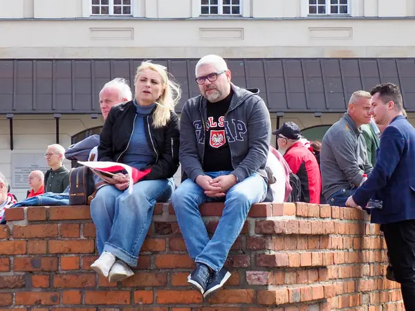 Bir grup yaşlı Polonyalı, tuğla duvarda oturmuş Varşova 'daki vatansever gösterisini izliyorlar.