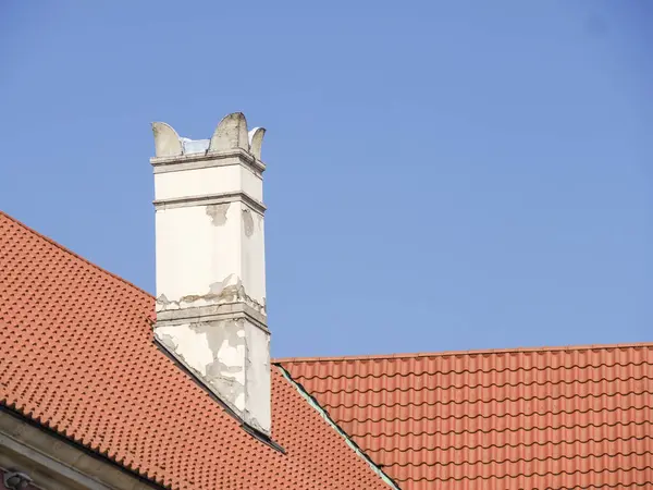 Terracotta çatı kiremitleri ve mavi gökyüzüne karşı dekoratif tacı olan geleneksel beyaz baca