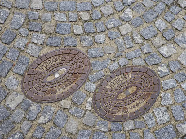 Geleneksel kaldırım taşlarına döşenmiş dekoratif desenli iki süslü bronz rögar kapağı.