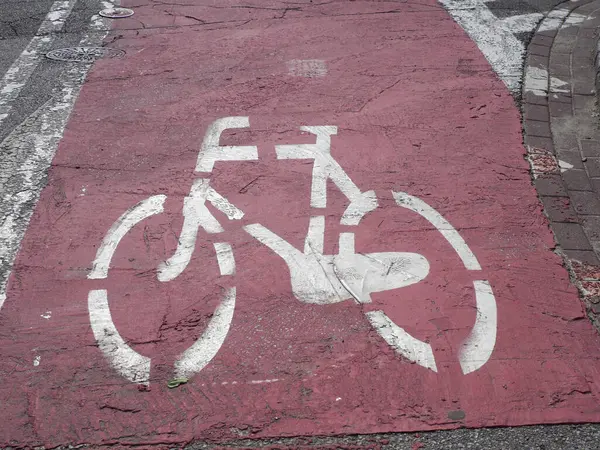 Yıpranmış kırmızı asfalt bisiklet yolu üzerinde şehir altyapısını gösteren beyaz bisiklet sembolü