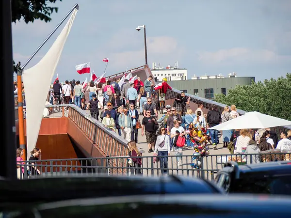 Kalabalık yaya köprüsü ve kırmızı korkuluklar yaz güneşinde yürüyen insanlarla doluydu.