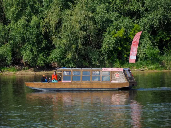 Geleneksel ahşap yolcu botu nehir kenarındaki iskeleye yanaştı. Pembe bayrak ve orman zeminiyle.