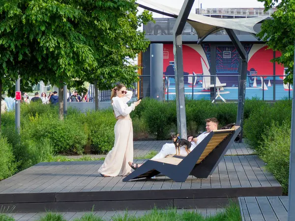 Modern ahşap şezlongda dinlenen beyaz elbiseli zarif kadın şehir parkı düzeninde.