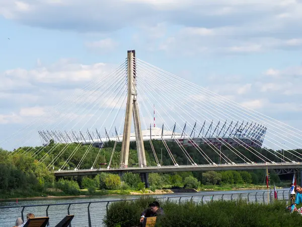Geniş nehir boyunca uzanan modern kablolu köprü şehir silueti ve bulutlu mavi gökyüzü