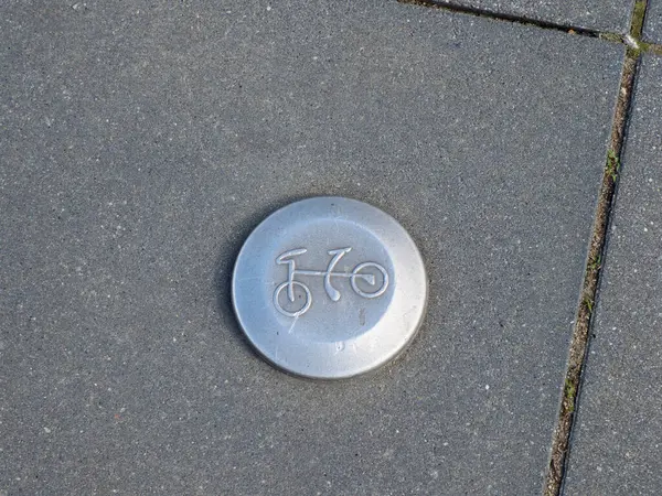 Görünür çatlak desenli asfalt yol yüzeyine gömülü metalik bisiklet sembolünün yakın plan ayrıntıları