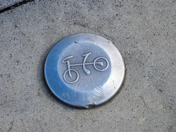 Beton kaldırım yüzeyine işlenmiş metal bisiklet sembolü kentsel bisiklet altyapısı ve sürdürülebilir ulaşımı gösteriyor