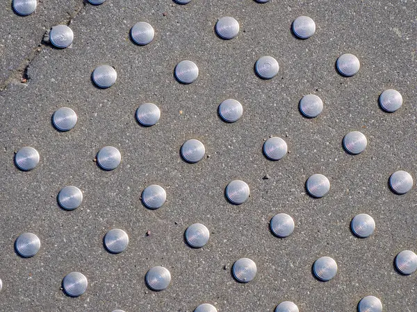 Beton yüzeyde sıra sıra dizilmiş dairesel metal çivilerin geometrik deseni modern kentsel dokuyu oluşturur