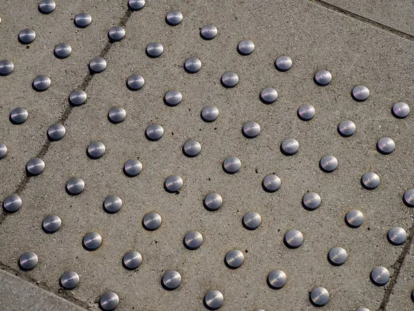 Beton kaldırım yüzeyindeki metal çivili desenler görme engelli yayalar için erişilebilirlik yolu oluşturuyor