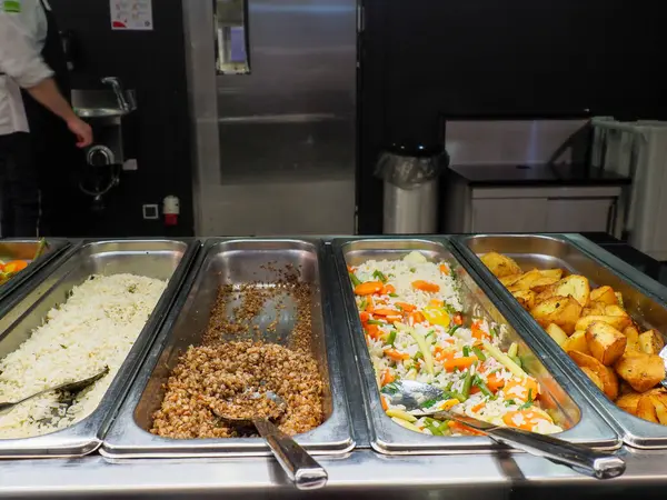 Endüstriyel kafeterya açık büfe kuyruğunda çoklu ısıtılmış servis konteynırları çeşitli hazır yiyecek seçenekleri sunuyor.