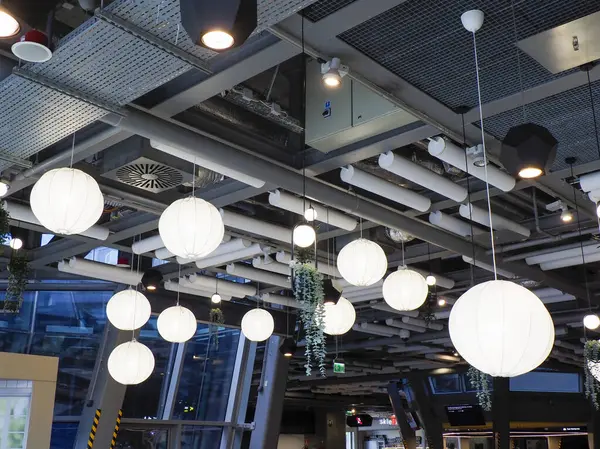 Geniş, modern restoran tavanında birden fazla beyaz dünya ışığı ve endüstriyel mimari unsurlar dramatik atmosfer yaratıyor.