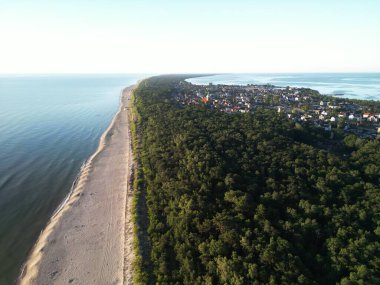 Açık mavi suların yanında orman kaplı yarımada boyunca yayılmış evler ile kıyı kasabasının göz alıcı manzarası.