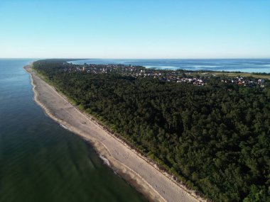 Çevresi el değmemiş sahil erişimi olan yemyeşil ormanlarla çevrili çarpıcı bir kıyı yerleşimi manzarası.