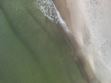 Turkuaz dalgaların kıyıları yıkadığı el değmemiş kumlu sahil manzarası doğal köpük desenleri yaratıyor.