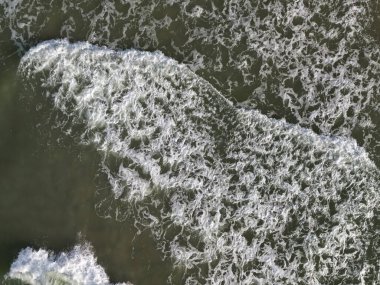 Köpüren beyaz okyanus dalgaları güçlü spreylerle çarpışarak dinamik su dokusu oluşturur.