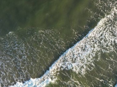 Okyanus yüzeyinin dramatik dron fotoğrafları yoğun dalga aktivitelerini beyaz köpükle koyu yeşil suyla çelişkili gösteriyor.