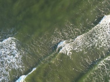 Sahil şeridine çarpan el değmemiş okyanus dalgalarının hava manzarası beyaz köpük desenleri yaratıyor.