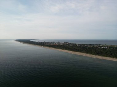 Karanlık sularla kaplı kıvrımlı kıyı tükürüğünün havadan görünüşü ve uzaktaki yerleşim alanı.