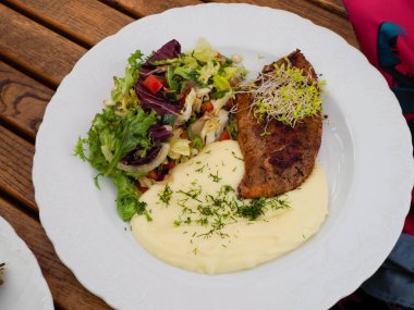 Bitki kabuklu patatesli birinci sınıf restoran bifteği ve beyaz seramik tabakta sanatsal tabakta karışık yeşil salata.