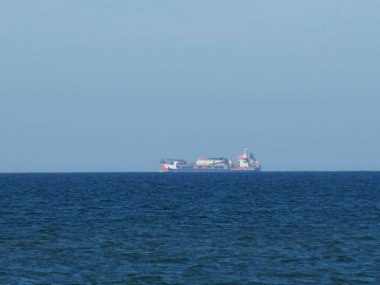 Büyük bir kargo gemisi, berrak gökyüzünün altında sakin mavi okyanus sularında yol alıyor.