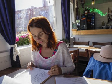 Genç bir kadın, sakin bir öğleden sonra çalışma saatinde rahat bir kafede kitap okur.