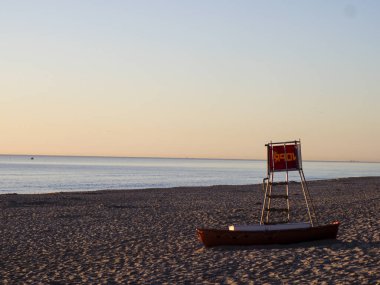 Turuncu cankurtaran gözlem kulesi engin boş kumsalda, altın saatinde, nazik dalgalarla.
