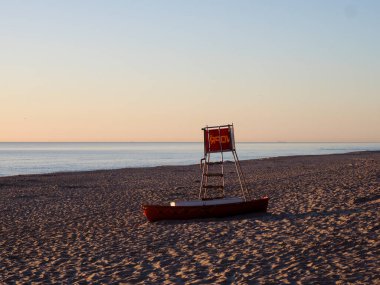 Gün batımında sakin Baltık Denizi sularıyla boş kumsalda duran kırmızı cankurtaran kulesi.