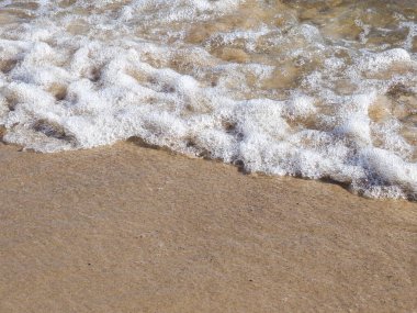 Köpüklü beyaz deniz dalgaları altın kumlu sahili ritmik gelgit hareketleriyle yıkıyor.