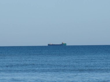 Uçsuz bucaksız gökyüzünün altında sonsuz mavi okyanus çizgisinde kargo gemisi silueti.