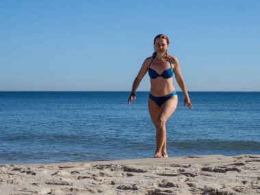 Atletik kadın mükemmel yaz gününde el değmemiş kumsalda neşeyle koşuyor.