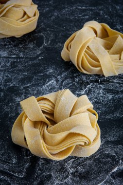 Pürüzsüz siyah bir bulaşık takımına üç sarı erişte konur. Zımba malzemesi lezzetli bir yemek ya da pişirilmiş yemek tarifi olarak pişirilmeye hazır.