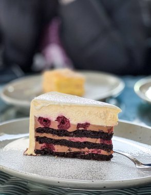 Pudra şekerli nefis bir dilim kek çatalın yanındaki tabakta duruyor. Bu pişirilmiş yiyecekler harika.
