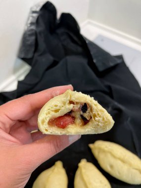 Bir insan elindeki ana yemeği gösteren, eksik bir ısırıkla bir hamur köftesi tutar. Hamur köftesi dutla dolu ve buğulanmış bir yemek olarak pişiriliyor.