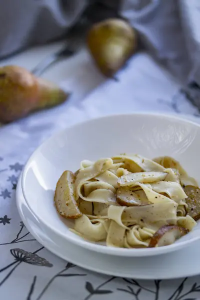 İçinde şehriye ve armut bulunan beyaz bir tabak. Masada güzelce yerleştirilmiş lezzetli bir karışım.