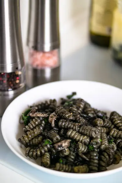 İtalyan mutfağında popüler bir yemek olan bir kase makarna biber değirmeninin yanındaki masada sergileniyor. Masa takımı tuz ve biber karıştırıcıları içeriyor.