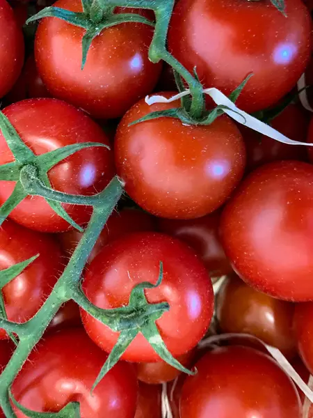 Bir demet olgun erik domatesi, canlı kırmızı renkli ve yeşil saplı bir çeşit çalı domatesi. Bu meyveler çeşitli yemeklerde popüler bir malzemedir ve doğal gıdalar olarak kabul edilir.