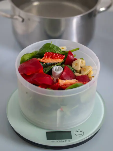 Yaprak sebze konteynırı, mutfaktaki bir tencere suyun yanında bir terazide durur. Malzemeler taze ve sağlıklı bir yemek tarifi için hazır.