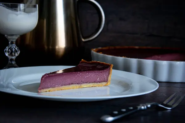 A purple pie slice sits on a white plate, ready to be enjoyed as a delicious dessert. The contrast of colors makes it visually appealing on the serveware