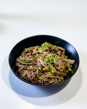 Beyaz bir masada siyah bir tabakta domuz etli, tatlı ve ekşi soslu karabuğday sobalı erişte. Yüksek kalite fotoğraf