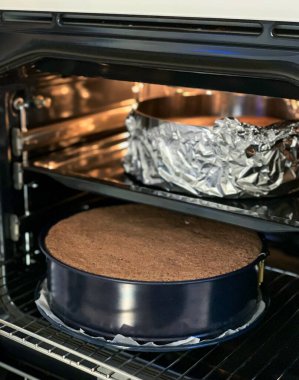 Yuvarlak bir pasta sergilenen çift katlı bir fırın ve alttaki folyoya sarılı başka bir lezzetli pasta.