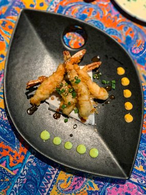 Bir tabak lezzetli karides tempura sanatsal olarak servis edilir, çeşitli renkli soslar eşliğinde.