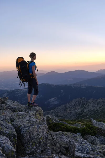 Gün batımında dağlarda yürüyüş kıyafeti giymiş gezgin bir kadın. Sırt çantalarıyla dağlarda yürüyüş yapıyorlar..