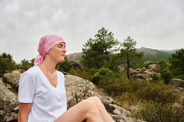 Woman with cancer closes her eyes while meditating and feels nature. She wears a pink scarf on her head