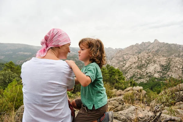 Woman with cancer relaxing in nature with her son. She wears a pink scarf on her head