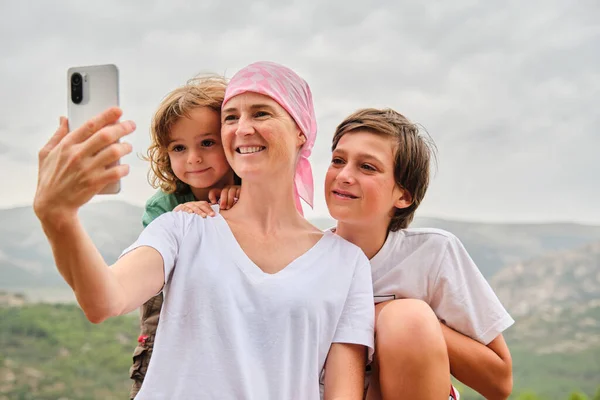 Woman with cancer taking a selfie with her family in the mountains.