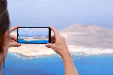 Kadın akıllı telefonuyla La Graciosa Adası 'nın fotoğrafını çekiyor. Lanzarote, Kanarya Adaları.