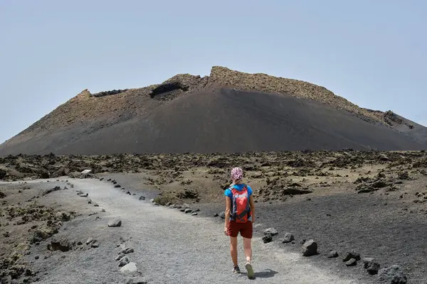 一个背着红色背包的女人走向兰萨罗特的埃尔库埃沃火山 加那利群岛 — 图库照片