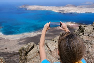 Kadın yürüyüşçü akıllı telefonuyla La Graciosa Adası 'nın tepesinden fotoğraf çekiyor. Kanarya Adaları