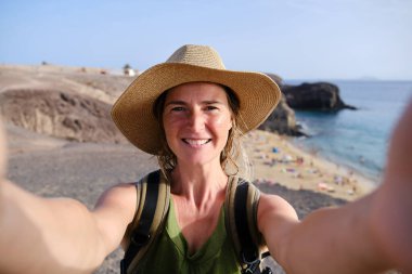 İspanya 'nın Lanzarote adasında arka planda Papagayo plajı ile selfie çeken kadın turist