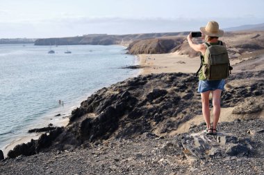 Lanzarote, Kanarya Adaları 'ndaki sahil şeridinde bir uçurumdan fotoğraf çeken turist kadın..