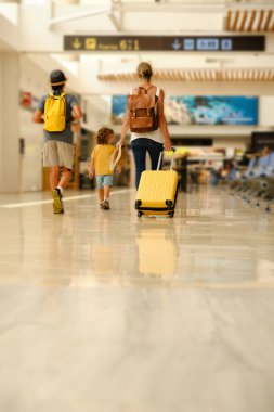 Bavullu anonim kadın ve sarı çantalı çocuklar modern havaalanındaki kalkış salonuna doğru yürüyorlar.